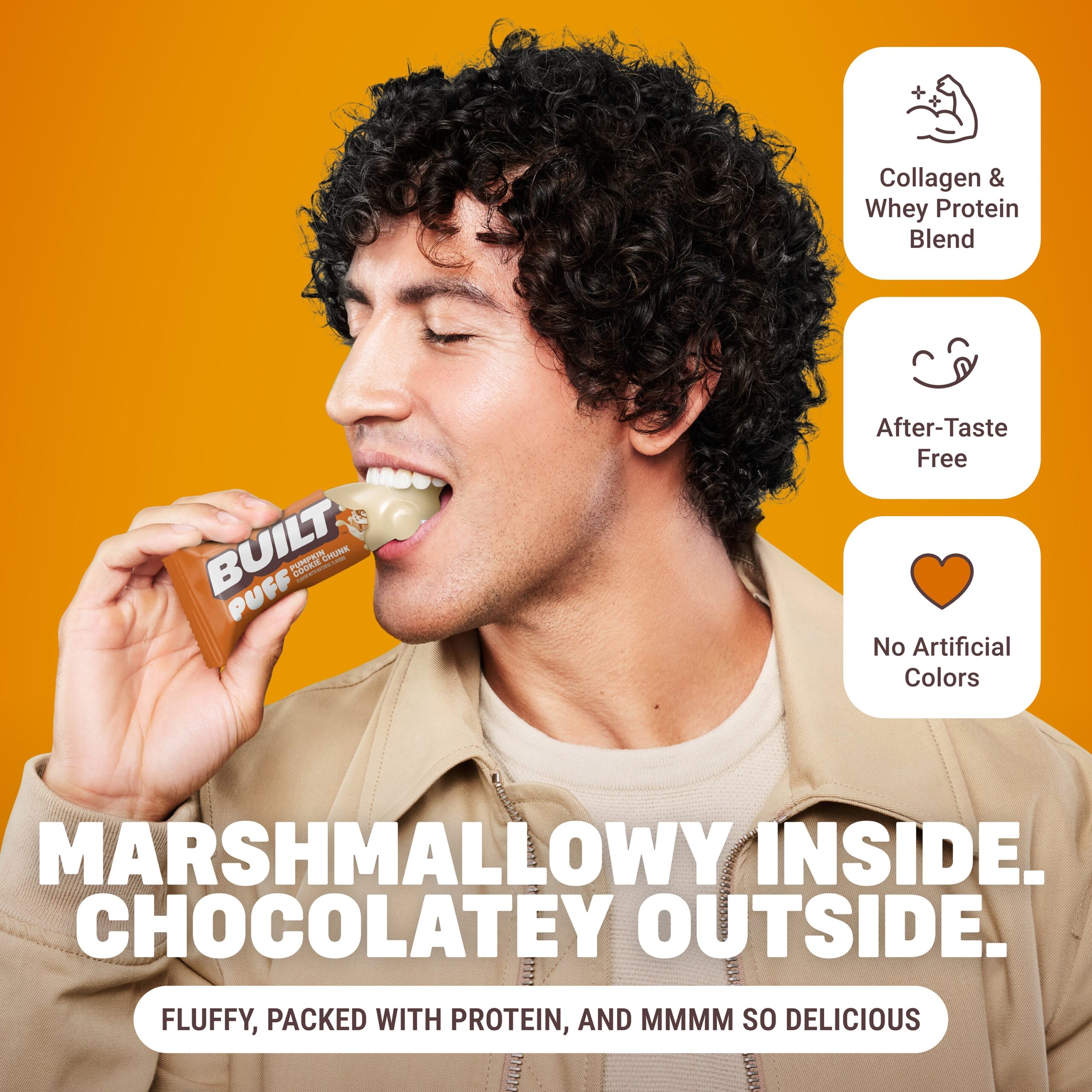 Man with curly dark hair eating a protein bar against yellow background with text about marshmallow interior and chocolate exterior