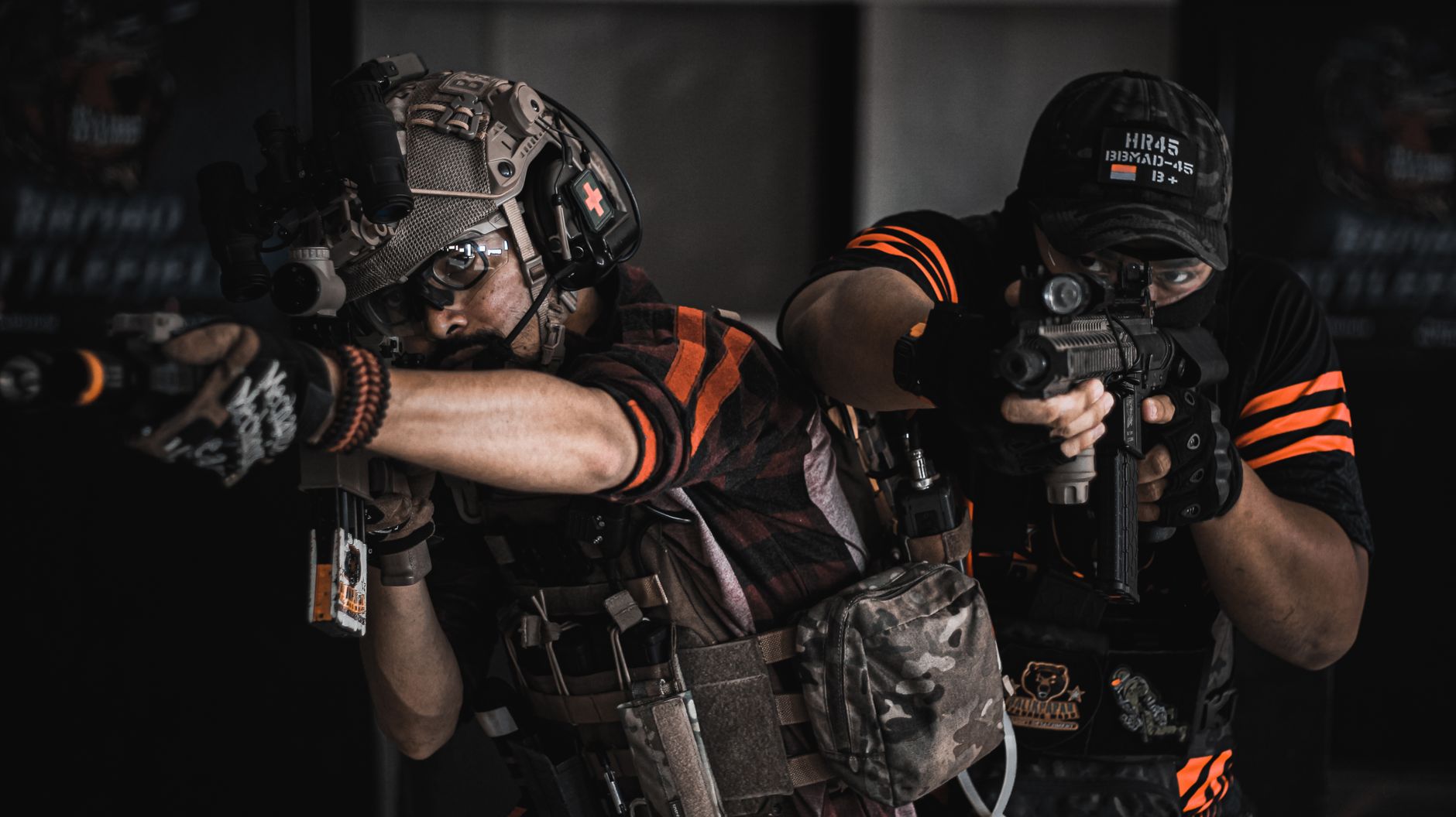 Dwaj gracze airsoft w czarno-pomarańczowym uniformie celują z replik broni podczas gry