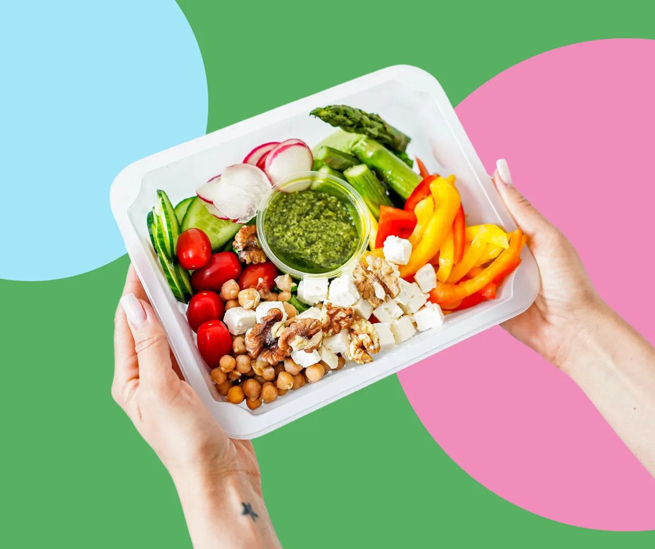 Dłoń trzymająca talerz z warzywami, orzechami, serem feta i sosem pesto