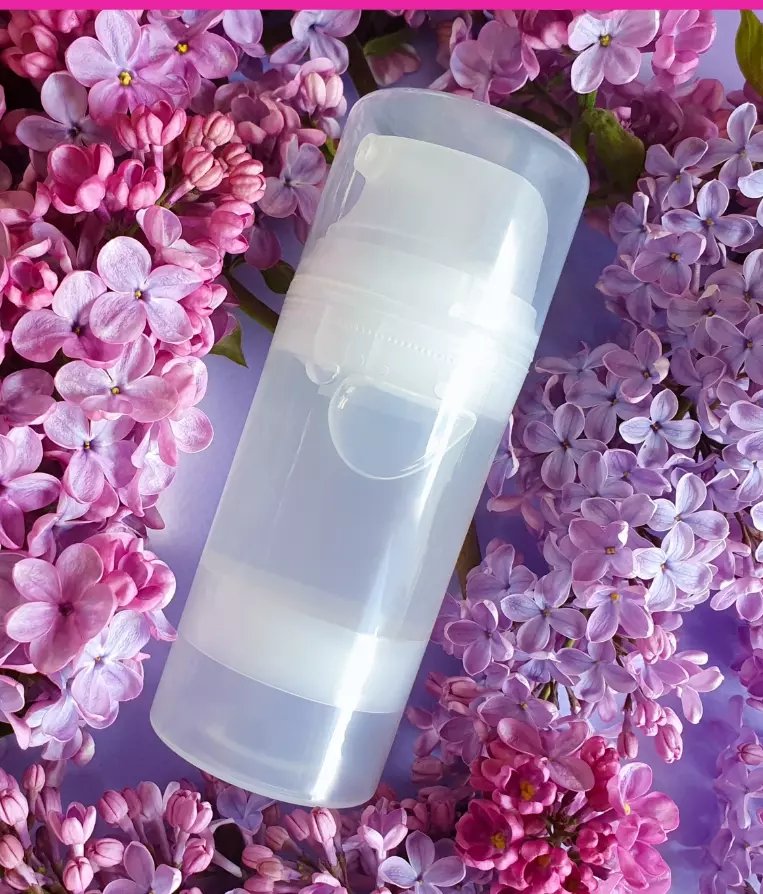 Transparente weiße Flasche mit Pumpspender zwischen rosa und violetten Blüten