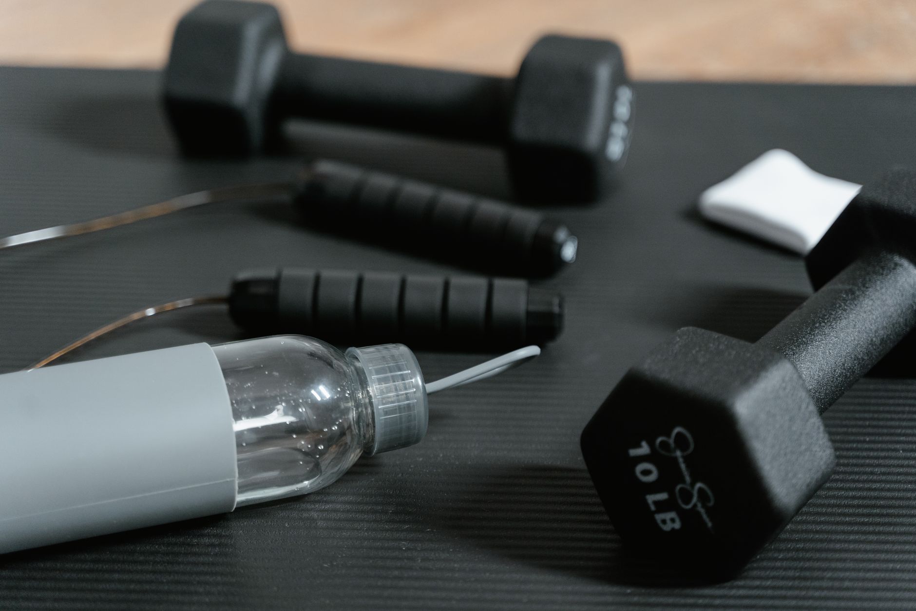 Sprzęt fitness na czarnym stole: hantelki, skakanka, butelka wody i ręcznik