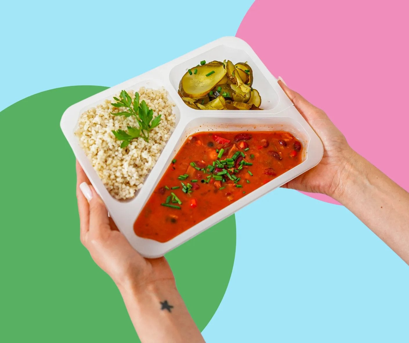 Dłoń trzymająca lunch box z kaszą, rosolą pomidorową i zapiekanką ze zucchini