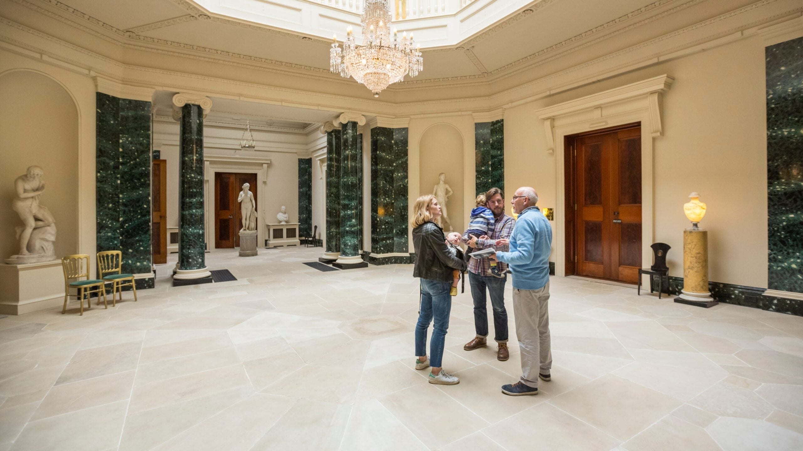 Adults and child in elegant interior hall with chandelier and classical columns
