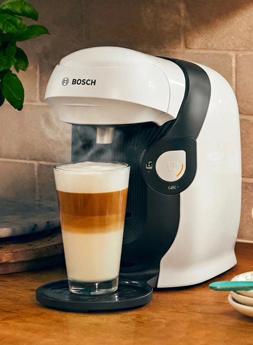 White and black single-serve coffee maker dispensing cappuccino into glass cup on wooden counter