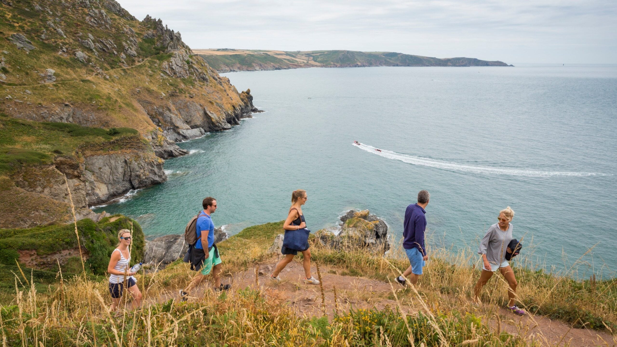 Group of runners jogging on coastal clifftop path overlooking turquoise sea