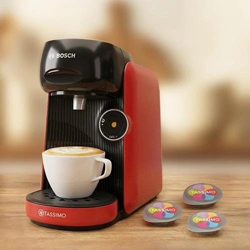 Red and black Bosch TASSIMO machine dispensing coffee with three colorful TASSIMO pods on wooden surface