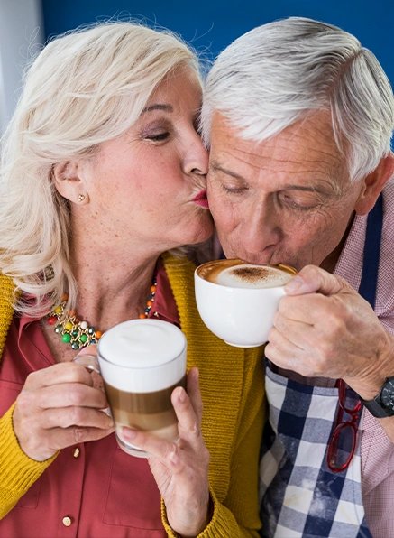 Older couple kissing while holding cups of coffee together