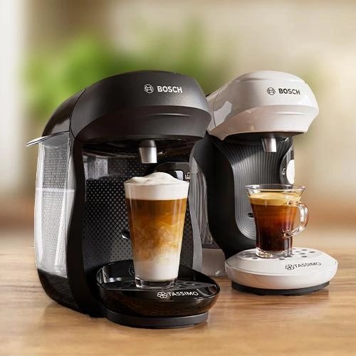 Two Bosch TASSIMO machines in black and white dispensing coffee into cups on wooden surface