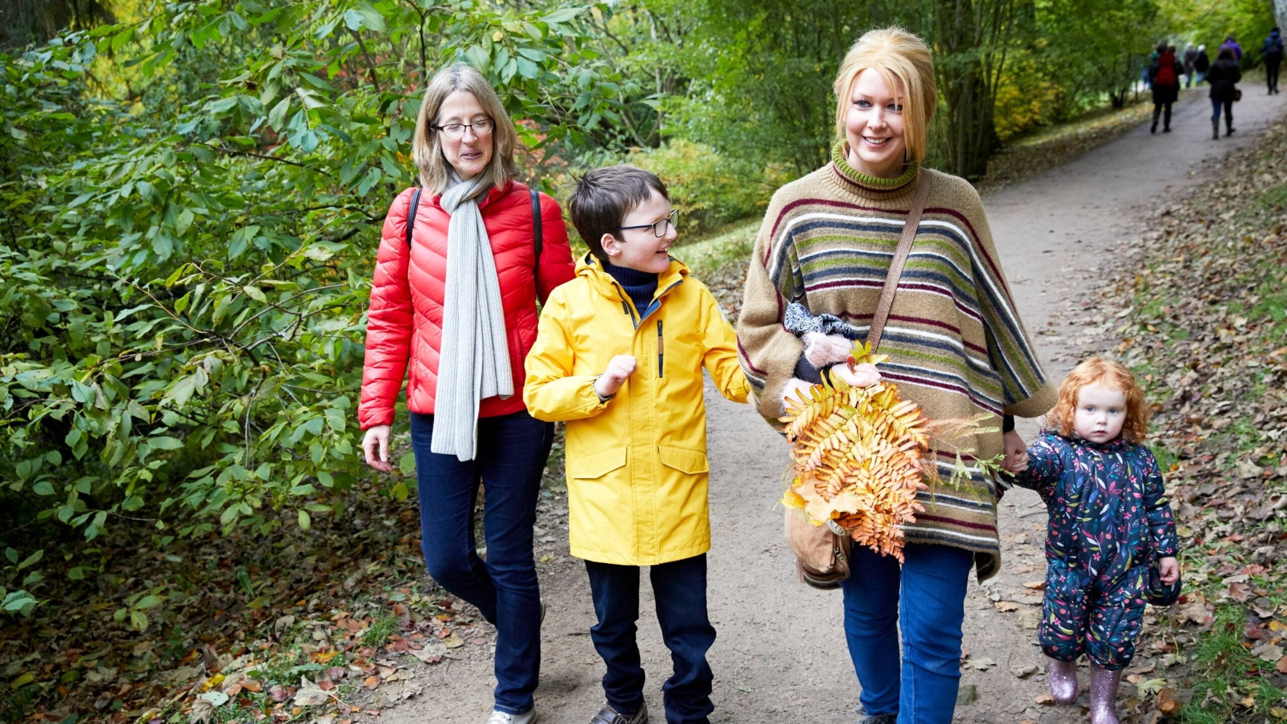 Family of five walking on a woodland path holding autumn leaves